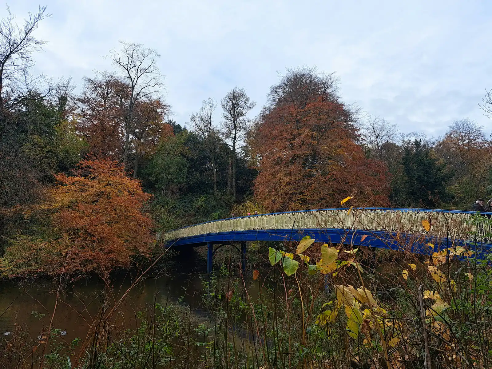 A blue footbridge crossing the River Kelvin among autumn trees on the riverside walkway in Glasgow