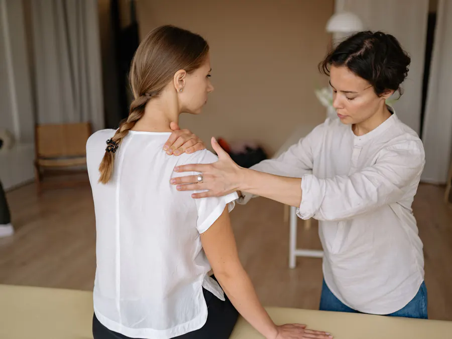 Physiotherapist giving hands-on treatment to a woman's painful shoulder and upper back