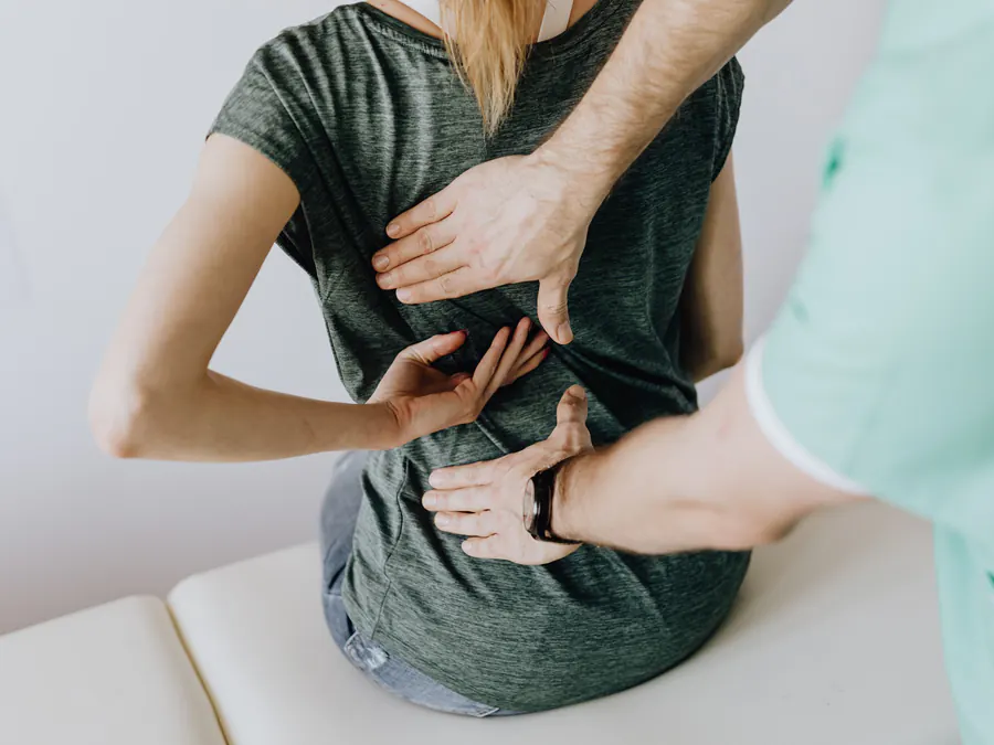 Clinician examining a woman's lower back as she points to a sudden, painful spot